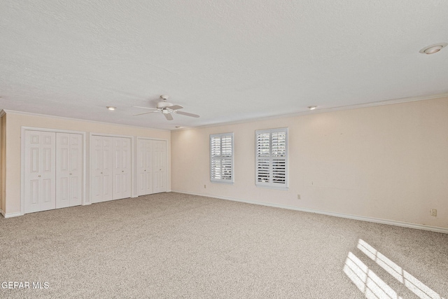 unfurnished bedroom with baseboards, carpet floors, ornamental molding, a textured ceiling, and two closets