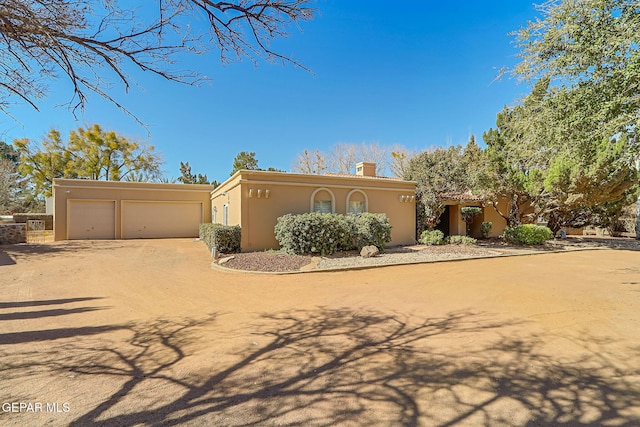 view of front of house with stucco siding, an attached garage, a chimney, and dirt driveway