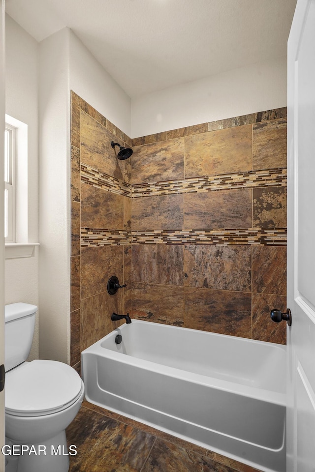 bathroom featuring tiled shower / bath combo and toilet