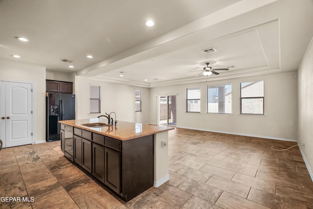 kitchen featuring a center island with sink, sink, ceiling fan, black fridge with ice dispenser, and dark brown cabinetry