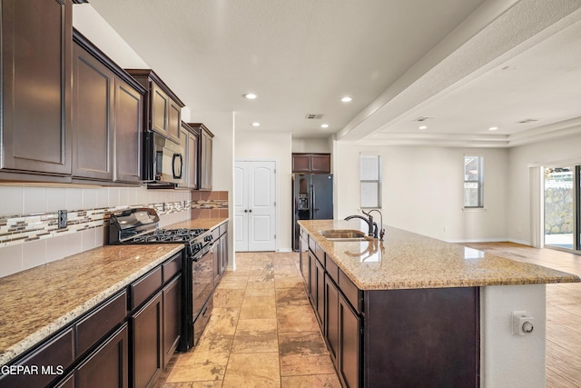 kitchen featuring light stone countertops, sink, backsplash, an island with sink, and black appliances