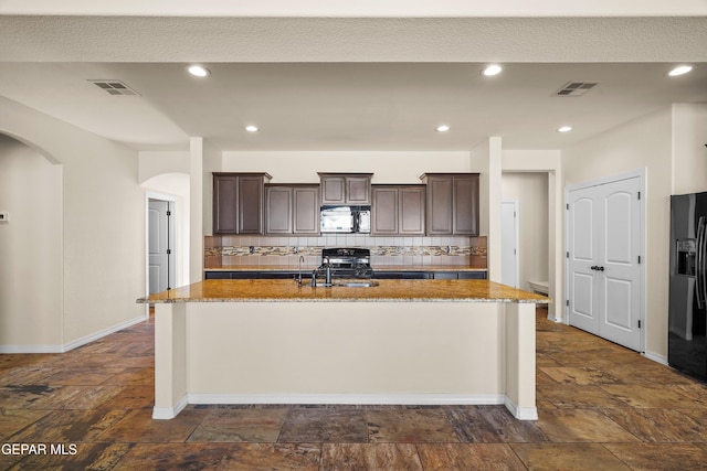 kitchen with decorative backsplash, dark brown cabinets, an island with sink, and black appliances