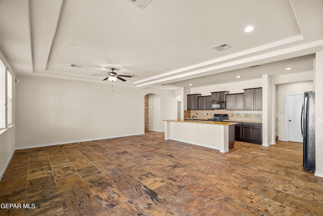 kitchen with ceiling fan, tasteful backsplash, a tray ceiling, dark brown cabinets, and black appliances