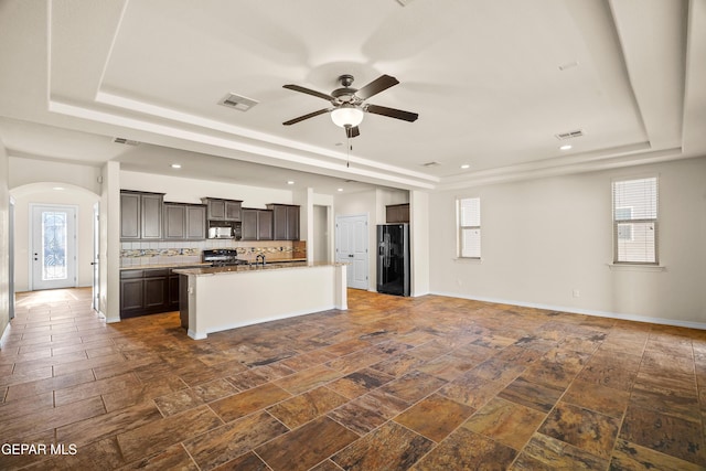 kitchen with a center island with sink, a raised ceiling, tasteful backsplash, and black appliances