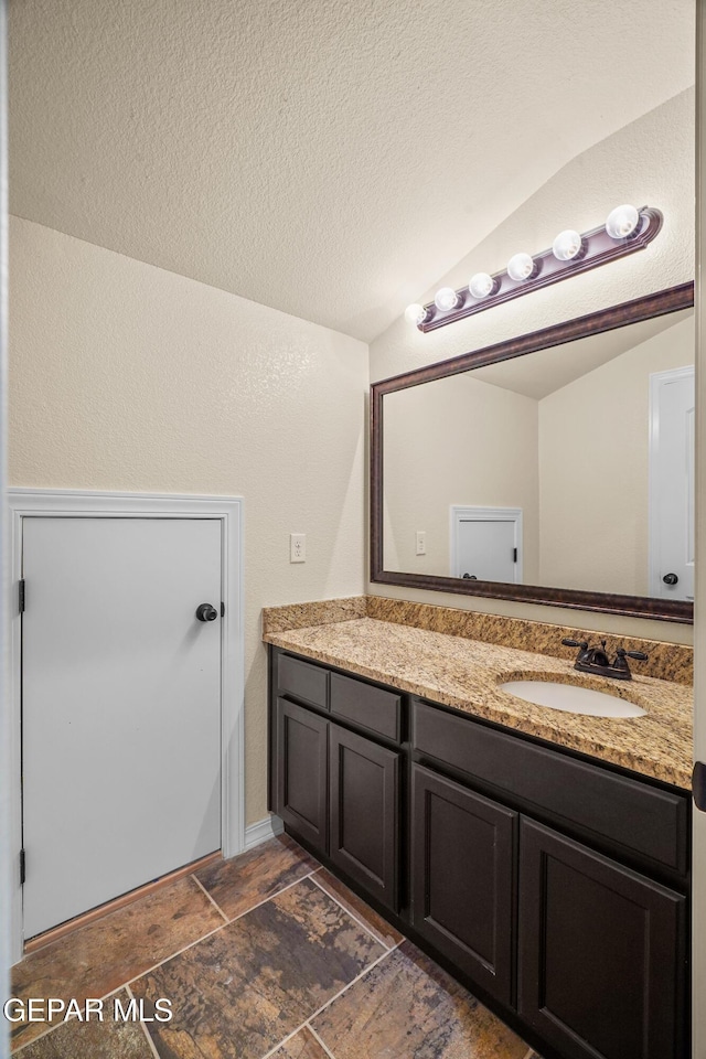 bathroom with a textured ceiling, vanity, and vaulted ceiling