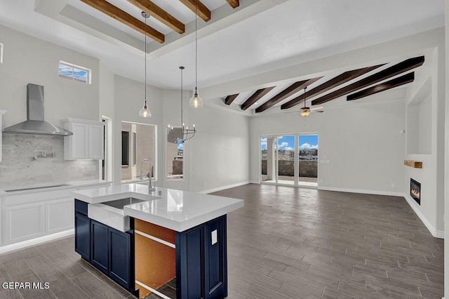 kitchen featuring blue cabinetry, white cabinetry, wall chimney exhaust hood, dark hardwood / wood-style flooring, and an island with sink