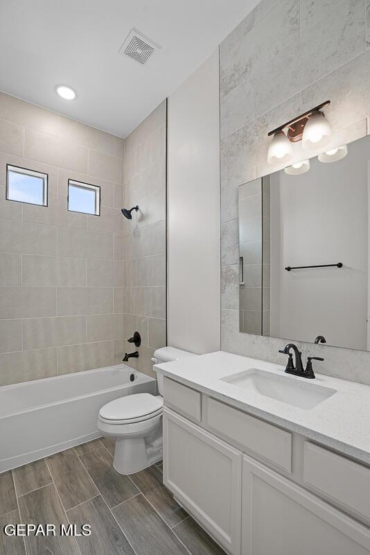 full bathroom featuring vanity, tiled shower / bath combo, and toilet