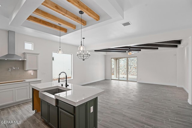 kitchen featuring sink, pendant lighting, a kitchen island with sink, decorative backsplash, and wall chimney range hood