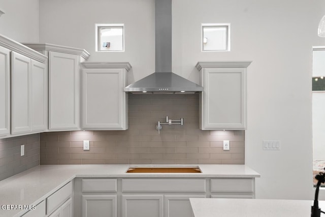 kitchen with stovetop, wall chimney range hood, white cabinets, and decorative backsplash