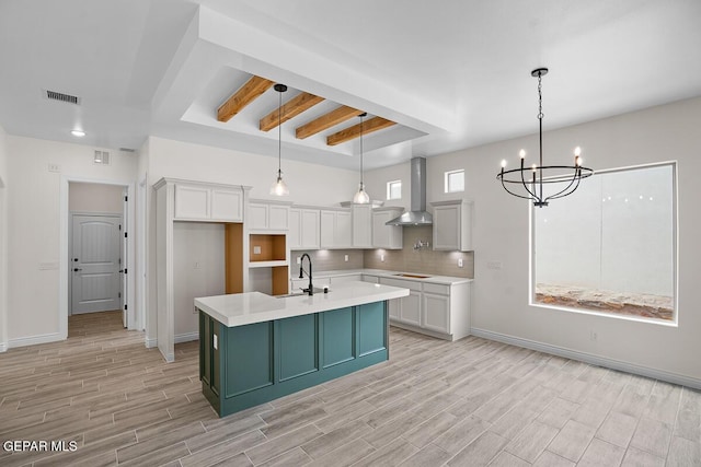 kitchen with sink, decorative light fixtures, a center island with sink, wall chimney range hood, and white cabinets