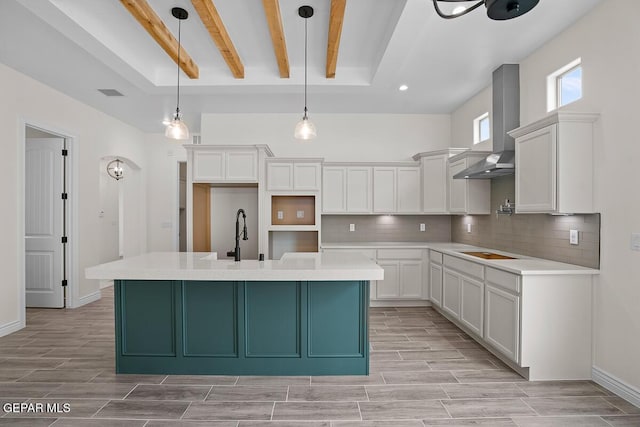 kitchen with white cabinetry, decorative backsplash, hanging light fixtures, wall chimney range hood, and a center island with sink