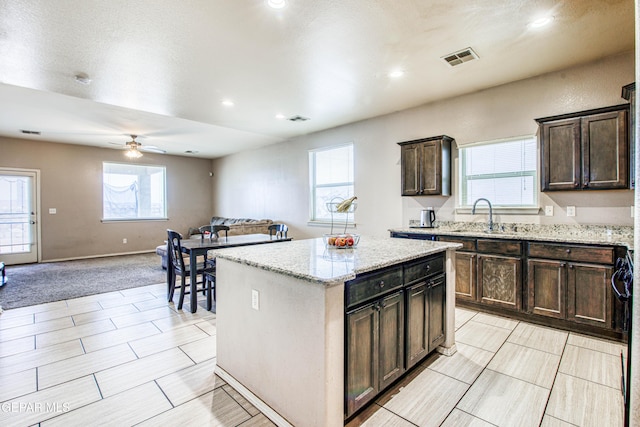 kitchen with light carpet, sink, ceiling fan, light stone countertops, and a kitchen island