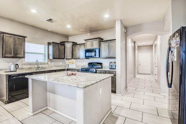 kitchen with black appliances, dark brown cabinets, a kitchen island, and light stone countertops