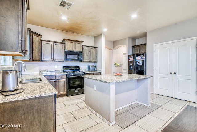 kitchen featuring sink, a center island, light stone countertops, and black appliances