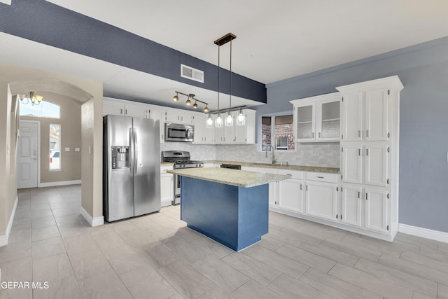 kitchen featuring white cabinetry, a center island, decorative light fixtures, decorative backsplash, and appliances with stainless steel finishes