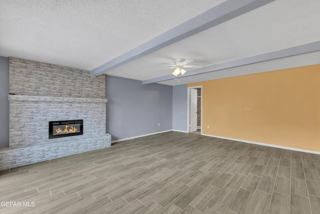 unfurnished living room with light wood-type flooring, a textured ceiling, ceiling fan, beamed ceiling, and a stone fireplace