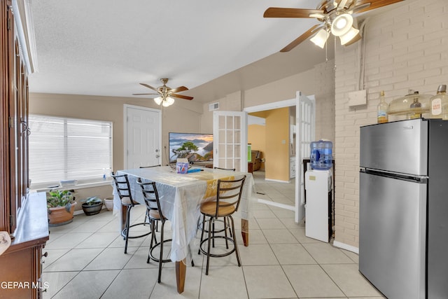 kitchen featuring stainless steel refrigerator, a textured ceiling, vaulted ceiling, a breakfast bar, and light tile patterned floors