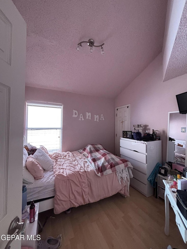 bedroom with light wood-type flooring, a textured ceiling, and vaulted ceiling