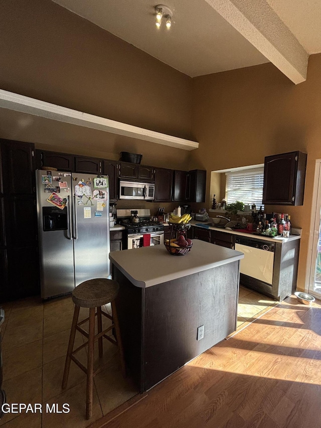 kitchen featuring appliances with stainless steel finishes, light wood-type flooring, a kitchen breakfast bar, dark brown cabinetry, and a kitchen island