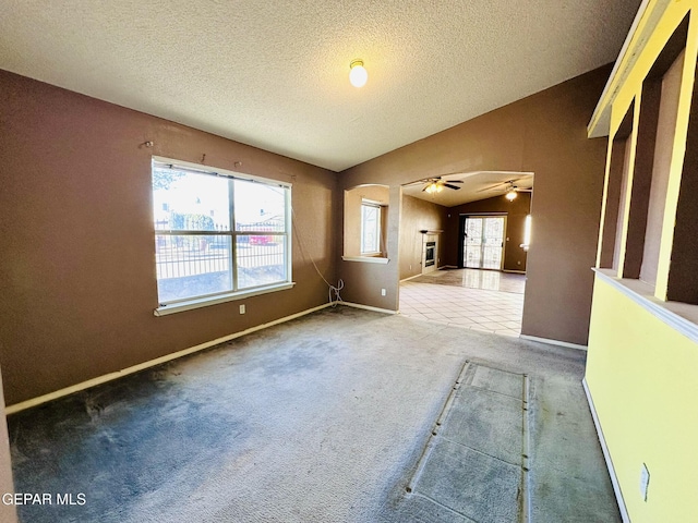 carpeted spare room featuring a textured ceiling, ceiling fan, a healthy amount of sunlight, and vaulted ceiling