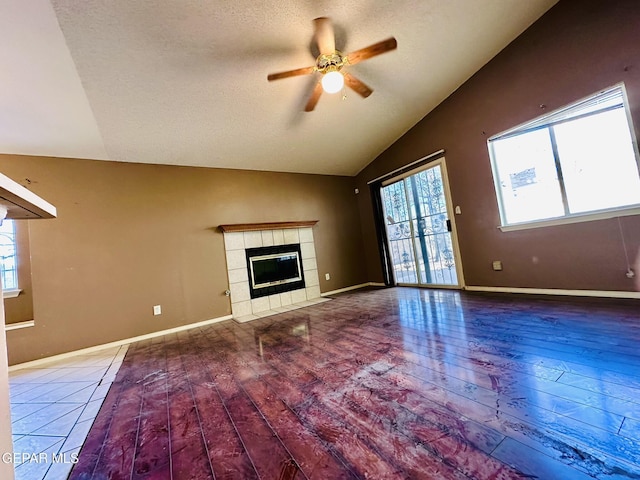 unfurnished living room featuring a textured ceiling, ceiling fan, a tile fireplace, hardwood / wood-style flooring, and lofted ceiling