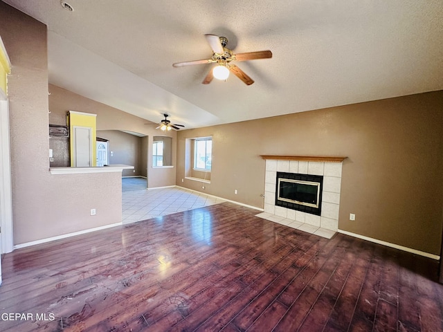 unfurnished living room featuring a tile fireplace, ceiling fan, hardwood / wood-style floors, and lofted ceiling