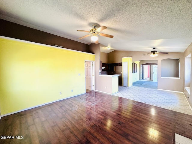 unfurnished living room with a textured ceiling, ceiling fan, light hardwood / wood-style flooring, and vaulted ceiling