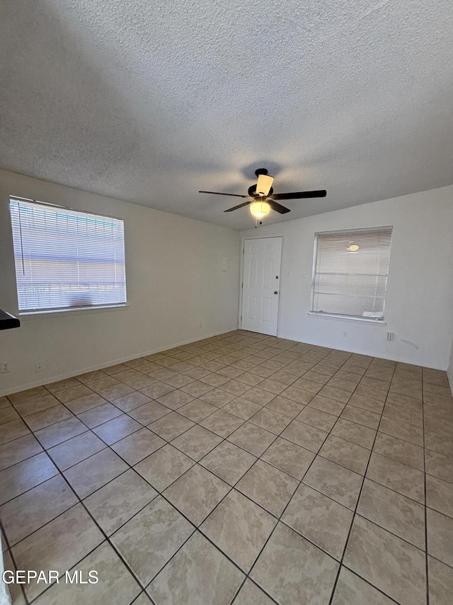 tiled empty room with ceiling fan and a textured ceiling