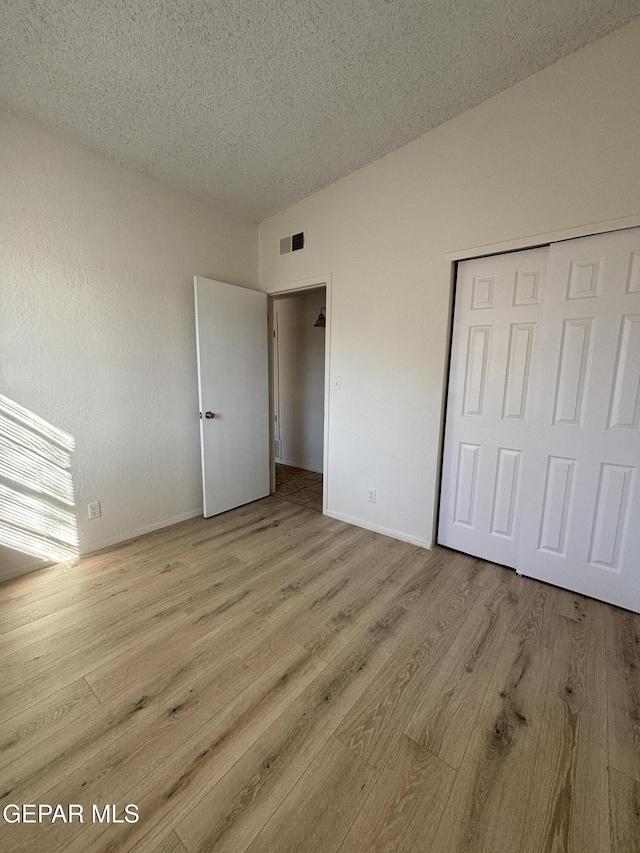 unfurnished bedroom with a closet, light hardwood / wood-style flooring, and a textured ceiling