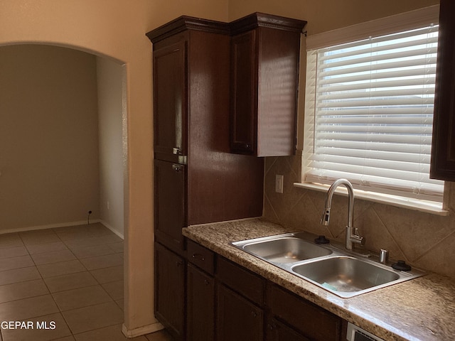 kitchen featuring decorative backsplash, dark brown cabinetry, sink, light tile patterned floors, and dishwasher