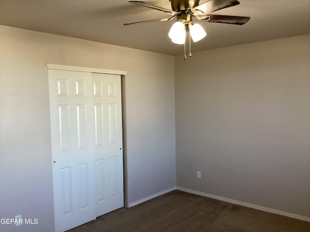 unfurnished bedroom featuring ceiling fan, dark carpet, and a closet