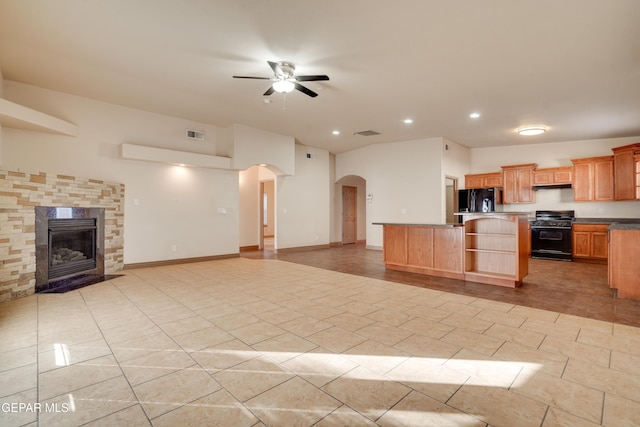 kitchen with gas range, black fridge, a kitchen island, ceiling fan, and a stone fireplace