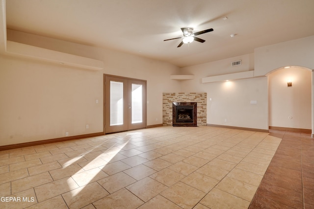 unfurnished living room with french doors, ceiling fan, light tile patterned floors, and a stone fireplace