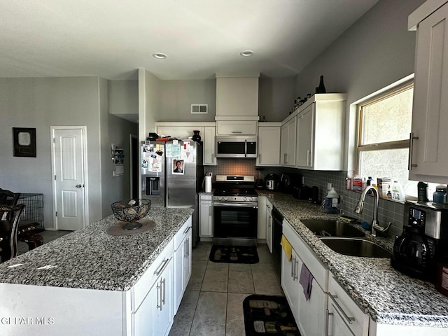 kitchen featuring white cabinets, sink, appliances with stainless steel finishes, stone countertops, and a kitchen island