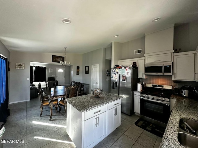 kitchen featuring a center island, white cabinets, light tile patterned floors, decorative light fixtures, and stainless steel appliances