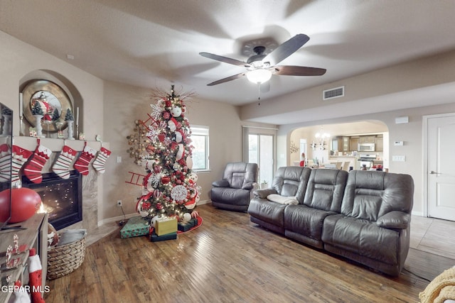 living room featuring a tile fireplace, hardwood / wood-style floors, and ceiling fan with notable chandelier