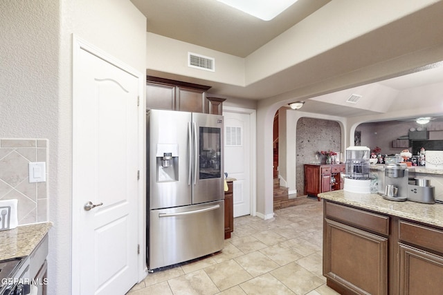 kitchen featuring light stone countertops, stainless steel fridge with ice dispenser, light tile patterned floors, and black range oven