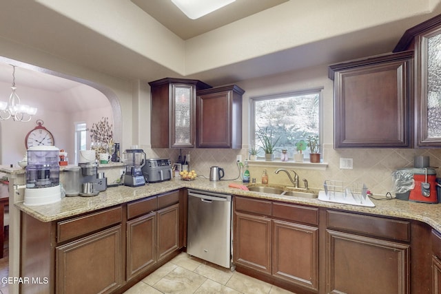 kitchen featuring decorative backsplash, light stone countertops, stainless steel dishwasher, sink, and a notable chandelier