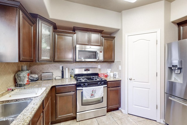 kitchen with appliances with stainless steel finishes, tasteful backsplash, light tile patterned floors, and light stone counters