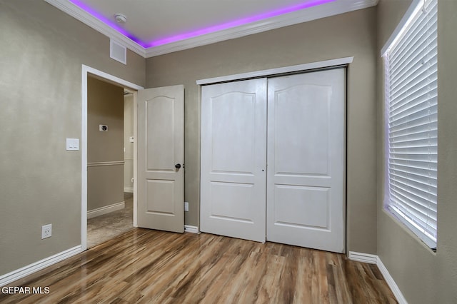 unfurnished bedroom with crown molding, a closet, and wood-type flooring