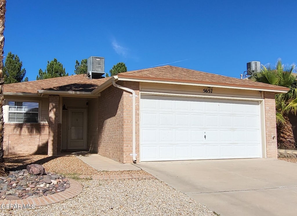 single story home with central AC unit and a garage