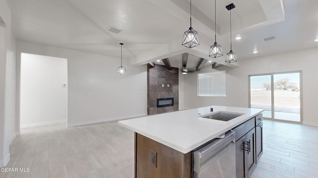 kitchen featuring dishwasher, a tile fireplace, a kitchen island with sink, and decorative light fixtures