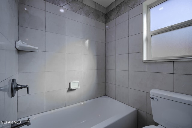 bathroom featuring toilet, tile walls, and tiled shower / bath