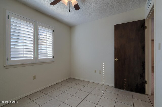 empty room featuring a textured ceiling, ceiling fan, and light tile patterned flooring