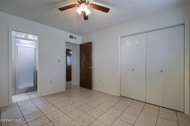 unfurnished bedroom with ceiling fan, light tile patterned floors, a textured ceiling, and a closet