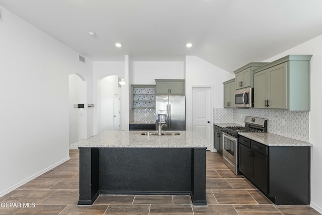 kitchen with light stone countertops, appliances with stainless steel finishes, backsplash, sink, and an island with sink