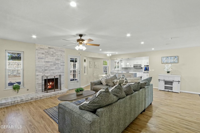 living room with ceiling fan, light wood-type flooring, a wealth of natural light, and a brick fireplace