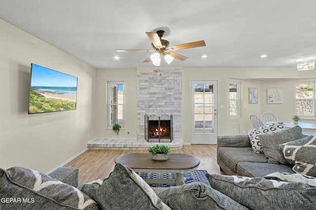 living room with a brick fireplace, ceiling fan, and light hardwood / wood-style flooring