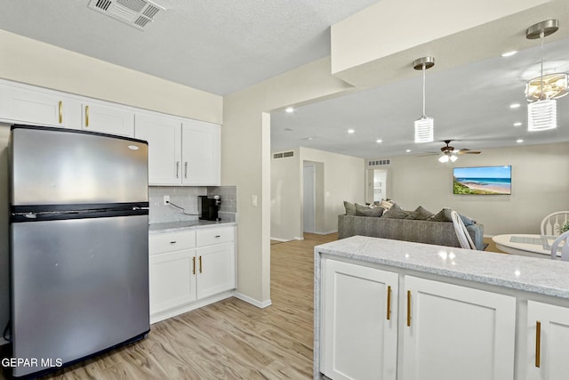 kitchen featuring white cabinetry, stainless steel fridge, hanging light fixtures, and light hardwood / wood-style floors