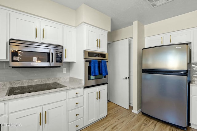 kitchen with tasteful backsplash, light stone counters, light hardwood / wood-style floors, white cabinets, and appliances with stainless steel finishes